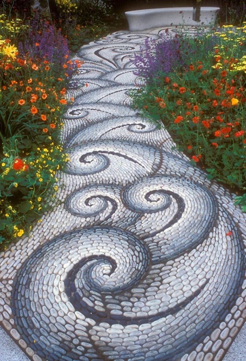 Stone walkway in the garden leading to a garden bench, with twists and twirls in pattern, along vibrant flower garden of red, yellow, orange, and purple, inlcuding Geum, Achillea, Salvia perennial plants creates feeling of movement and excitement